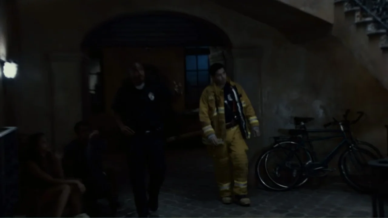 Quarantine (2008) movie still: medium — A stone-walled courtyard at night features an arched entryway and stairs to the side. A firefighter and…
