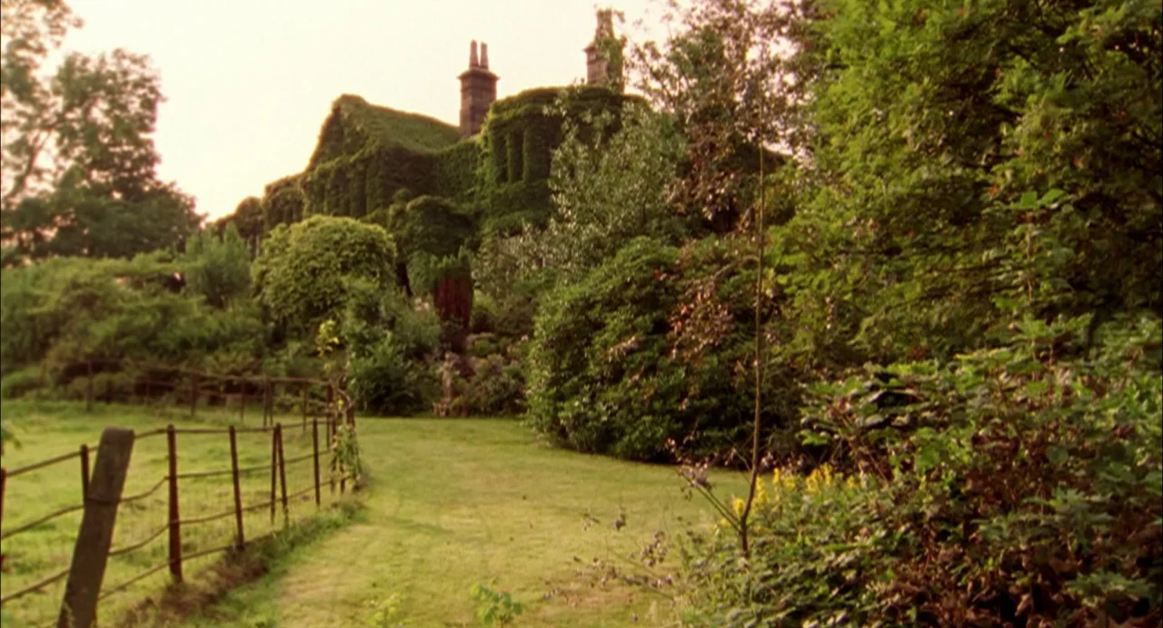 My Summer of Love movie still: establishing — A large stone manor house is completely covered in thick green ivy vines. A grassy path leads through…
