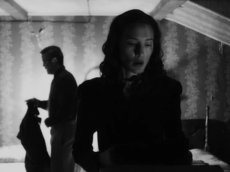 The Good German movie still: A tense, quiet moment between a couple in a cramped, dimly lit bedroom. The high-contrast black and white photography…