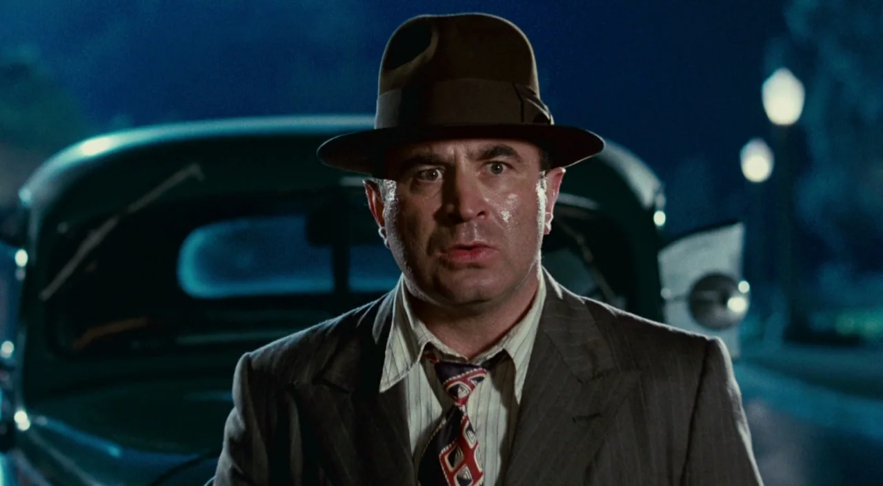 Who Framed Roger Rabbit (1988) movie still: closeup — A man stands outdoors at night in front of a dark vintage automobile. He faces the camera…