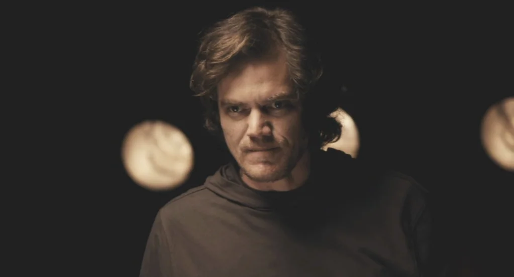 My Son, My Son, What Have Ye Done? (2009) movie still: medium — A man stands centered in a dark, indistinct environment with out-of-focus background…
