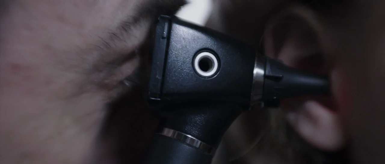 The Babadook (2014) movie still: closeup — A close-up view shows an otoscope positioned against an ear. A person looks through the medical instrument.