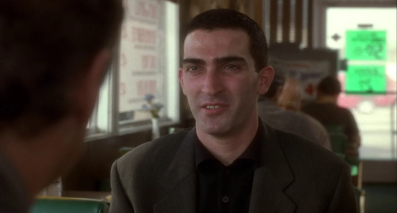 Mulholland Drive (2001) movie still: medium — A man sits in a booth inside a diner with green upholstery. He is looking at an unseen person seated…