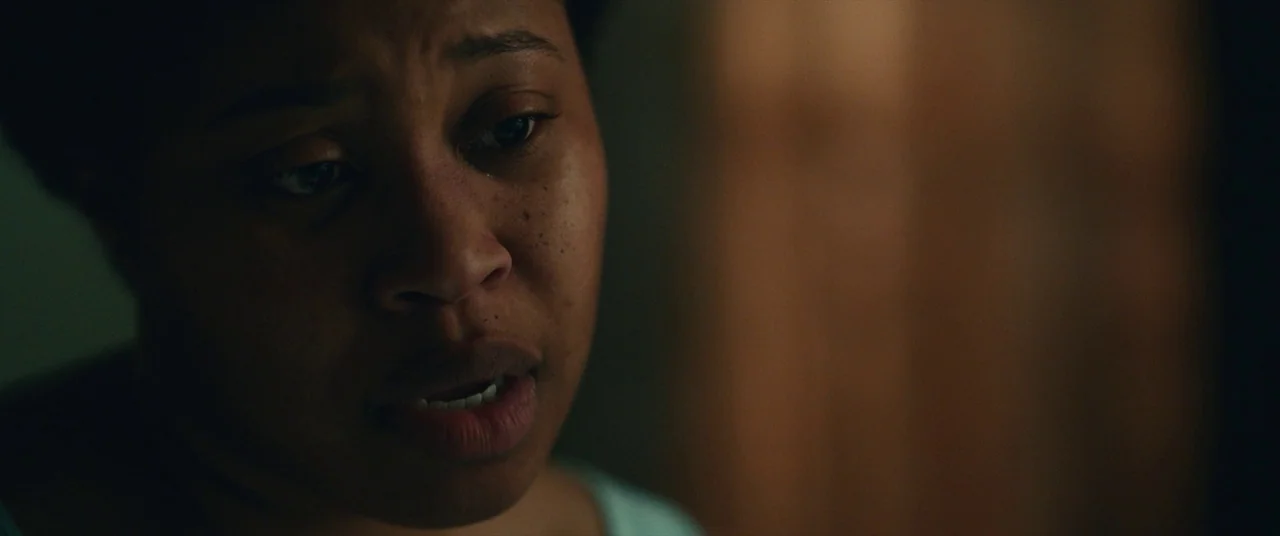 Judas and the Black Messiah (2021) movie still: closeup — A dimly lit room with out-of-focus background textures in shadow. A woman stares…