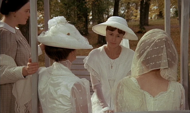 Cries and Whispers (1972) movie still: medium — Four women in early 20th-century attire gather inside a wooden outdoor structure. They sit and stand…