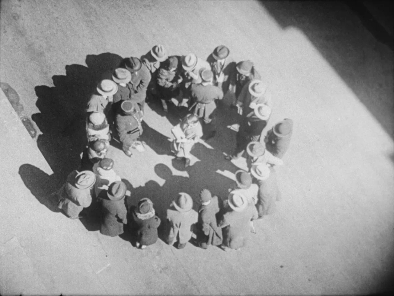 Un Chien Andalou (1929) movie still: wide — A large crowd of people in winter coats and hats forms a circle outdoors. One person stands in the…