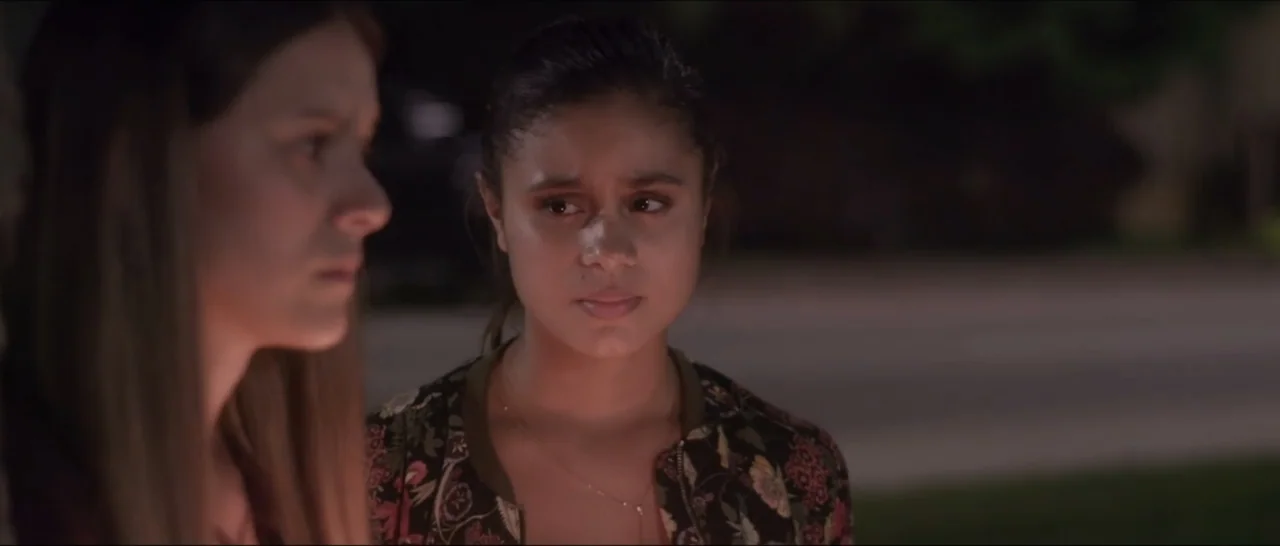 If You're Gone (2019) movie still: medium — A dark residential street at night serves as the backdrop for two women. One woman faces the camera…