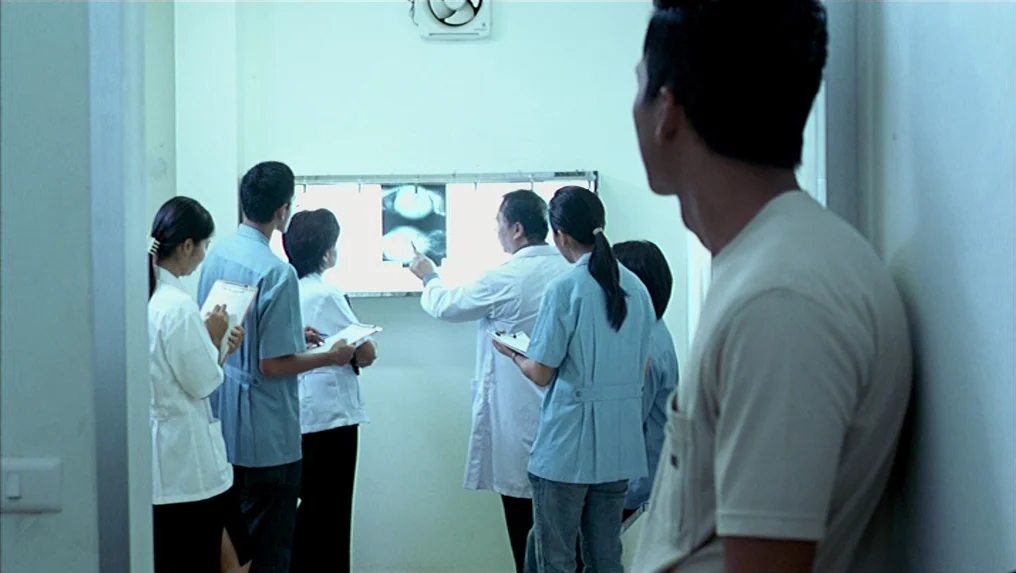 Tropical Malady (2004) movie still: medium — A group of medical personnel gathers in a sterile, light-walled hallway to review scans. A doctor leads…