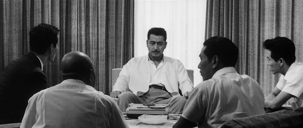 High and Low (1963) movie still: medium — A group of five men sit in chairs facing a central figure in a room. The room has heavy pleated…