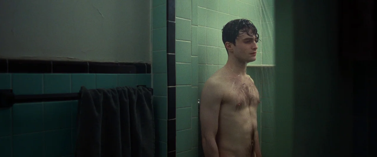 Kill Your Darlings (2013) movie still: medium — A tiled interior room features dark teal square tiles and a hanging towel. A young man with wet hair…