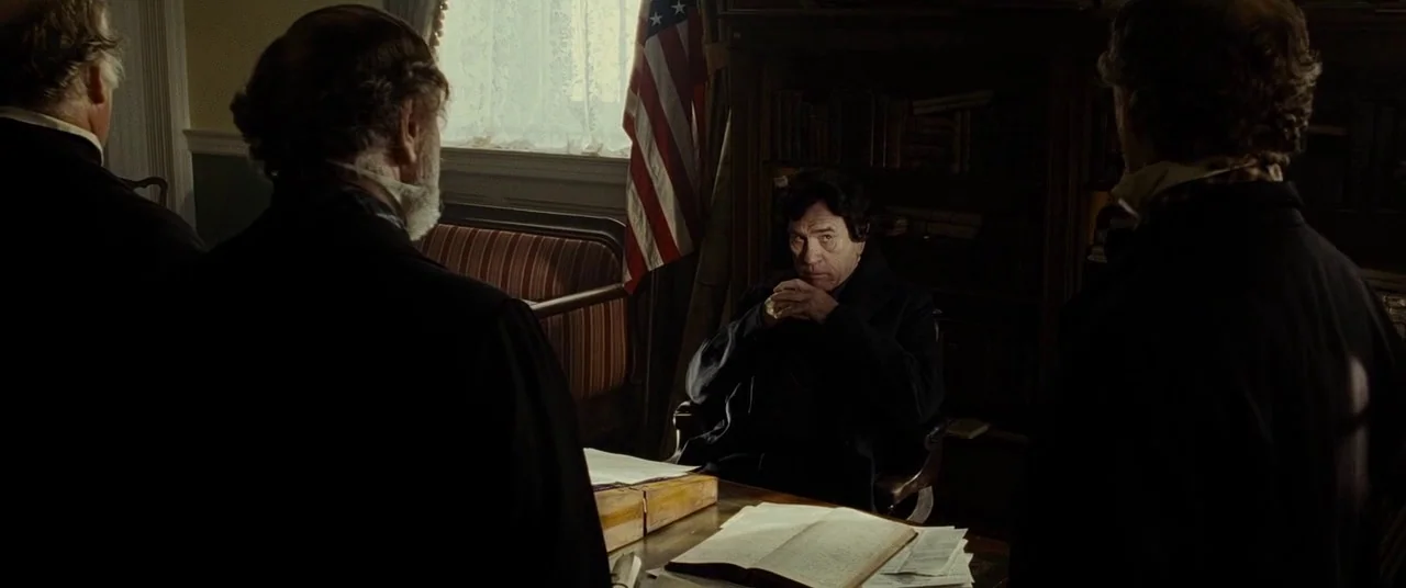Lincoln (2012) movie still: medium — A 19th-century private study contains wooden bookshelves and a desk with open ledger books. A man sits at the…