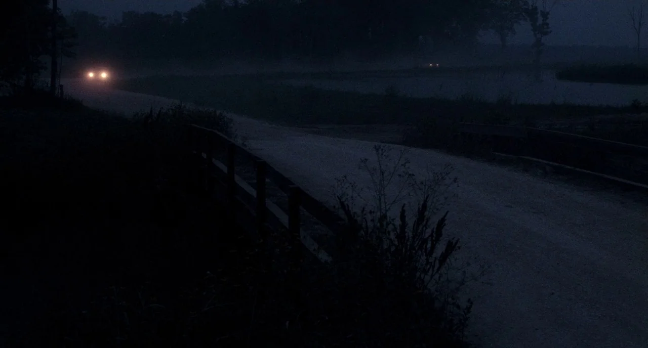 Angel Heart (1987) movie still: wide — A rural dirt road stretches through a dark, foggy landscape at night. A vehicle with active headlights…