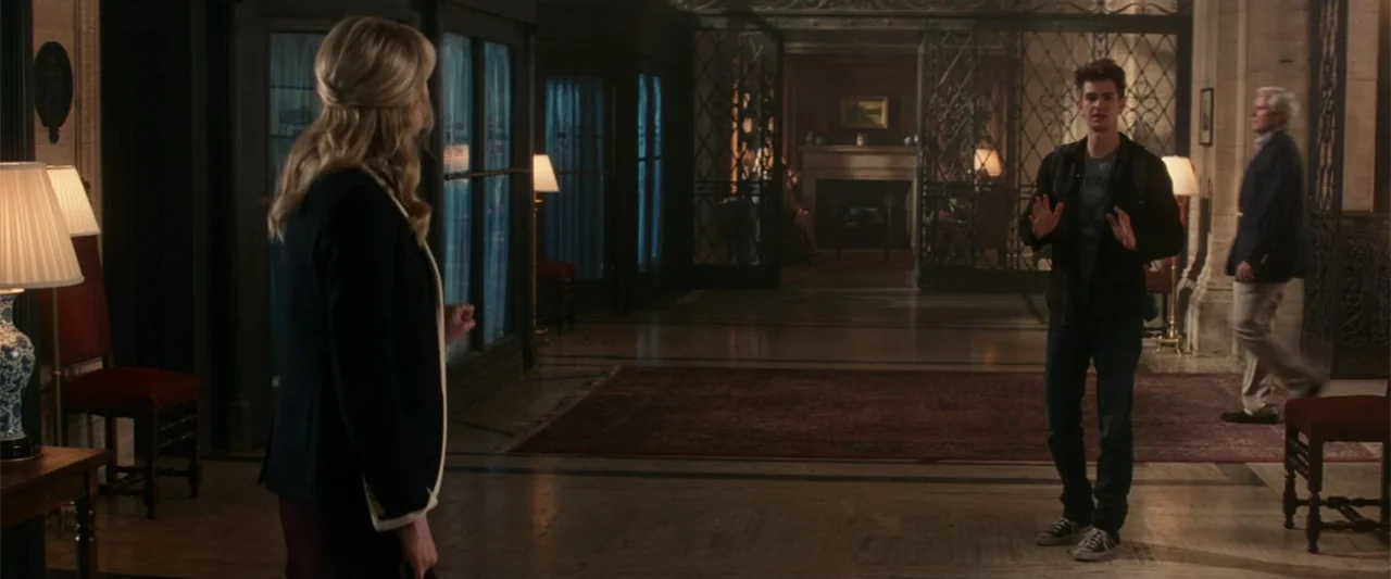 The Amazing Spider-Man 2 (2014) movie still: medium — A stone-walled corridor features an ornate iron gate and a red patterned area rug. A young man…