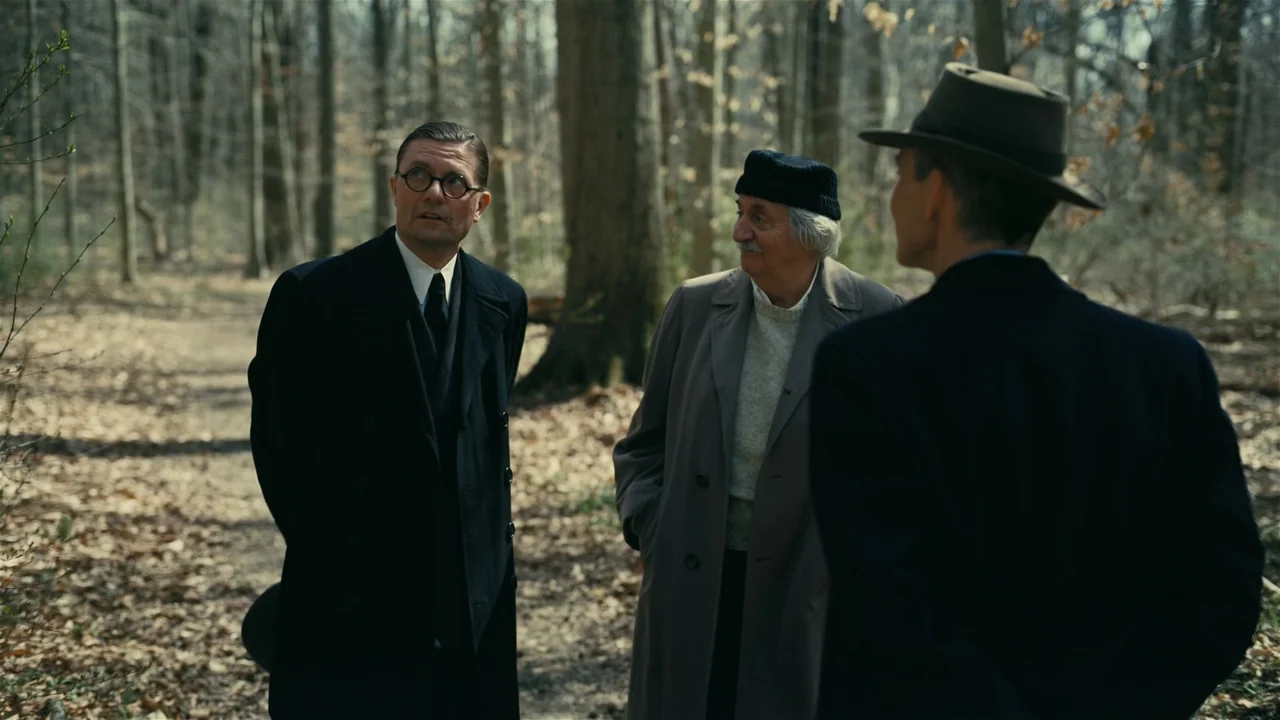 Oppenheimer (2023) movie still: fullbody — A group of men stand on a dry dirt path surrounded by bare winter trees. The individuals wear vintage…
