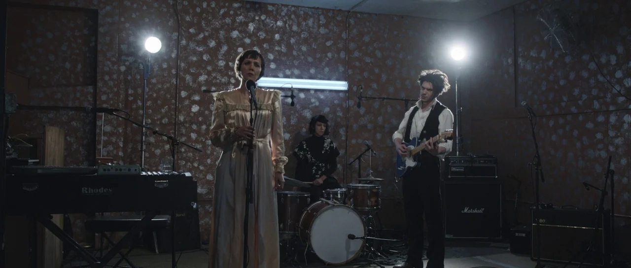Frank (2014) movie still: fullbody — A dimly lit room with textured, brown, spotted walls serves as a rehearsal space. A band consisting of a…