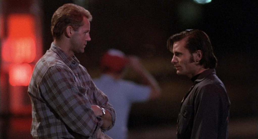 The Indian Runner (1991) movie still: medium — Two men face each other in a dark urban parking lot at night. One man in plaid shirt talks to another…
