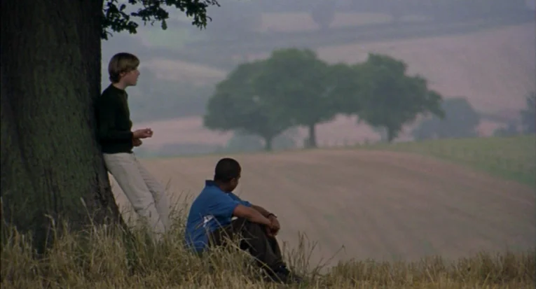 A Room For Romeo Brass (1999) movie still: fullbody — Two teenagers rest in a rural field next to a large, gnarled tree. Rolling hills with distant…