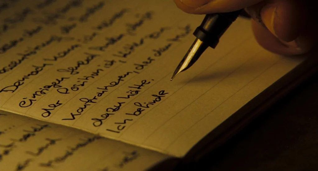 Valkyrie (2008) movie still: closeup — A close-up view of handwritten German text on white lined paper in a journal. A black fountain pen held by a…
