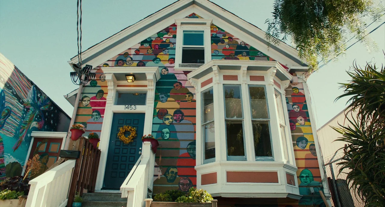 Blindspotting (2018) movie still: wide — A residential house exterior features a colorful mural of faces painted across the siding. The building has…