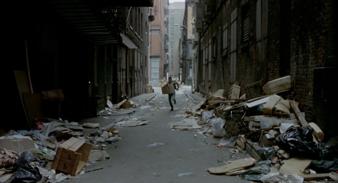 Ms. 45 (1981) movie still: wide — A trash-filled city alleyway is lined with brick buildings and fire escapes. A lone man runs forward down the…