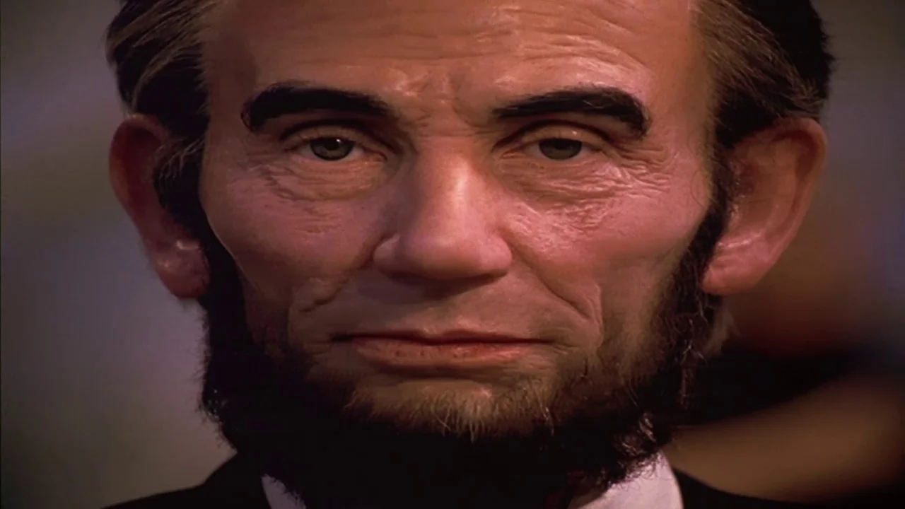 Naqoyquatsi (2002) movie still: closeup — A close-up of a statue resembling Abraham Lincoln within a stone memorial hall. The subject stares ahead…