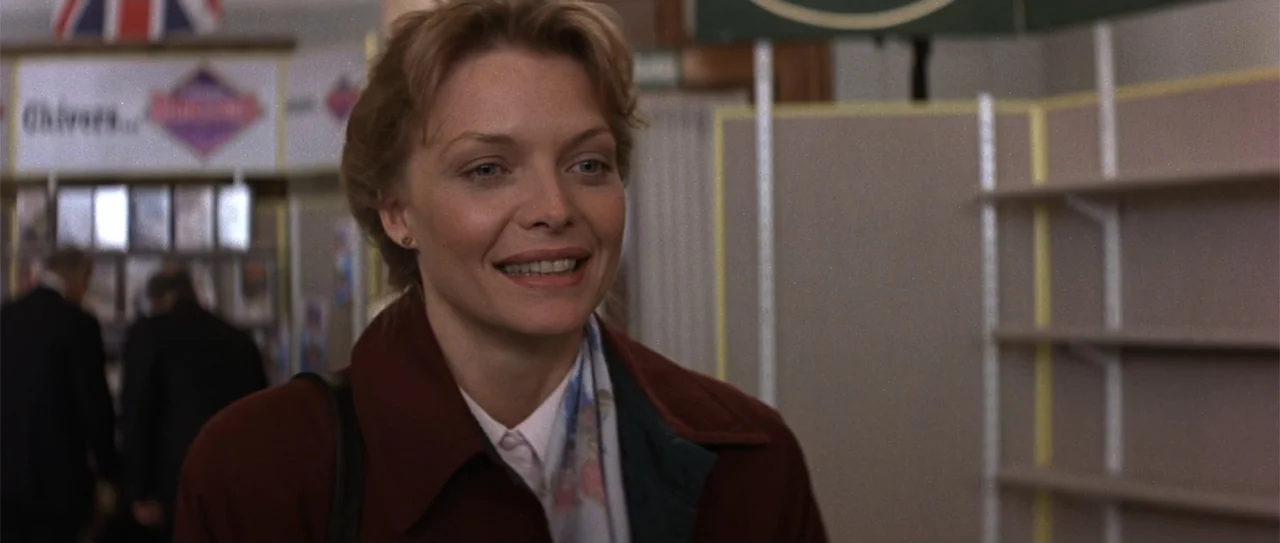 The Russia House (1990) movie still: medium — An indoor retail environment with shelving units and signage in the background. A woman in a maroon…