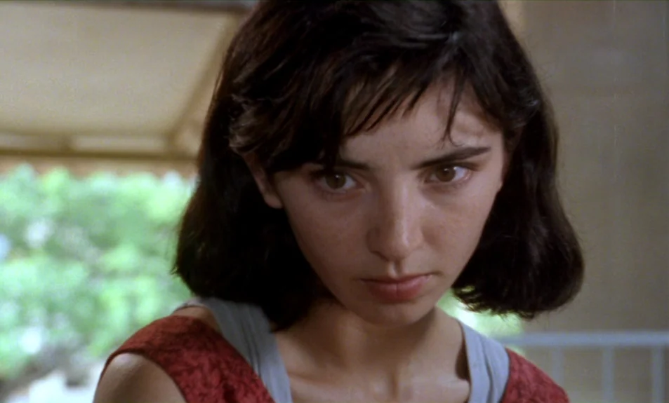 Casa De Lava (1994) movie still: closeup — A woman stands outdoors near a white railing with blurred green foliage behind her. She faces forward…