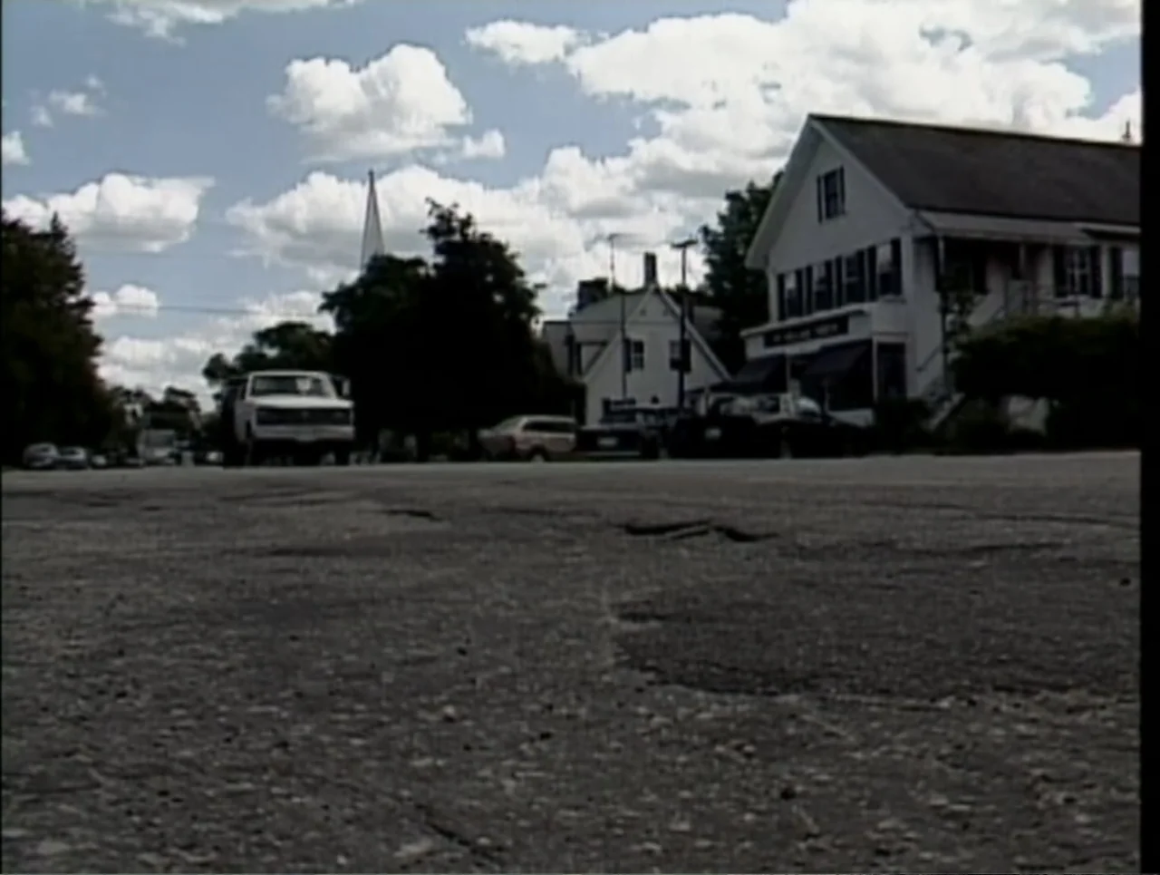 A Rape in a Small Town: The Florence Holway Story (2005) movie still: establishing — A rural main street features asphalt pavement with parked cars…