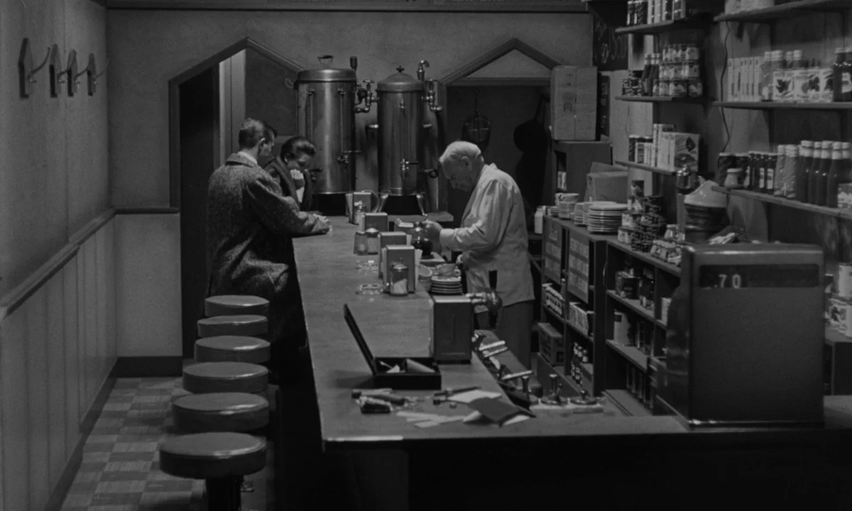 Sweet Smell of Success (1957) movie still: wide — A 1950s style diner counter displays shelves packed with canned goods and glass bottles. The…