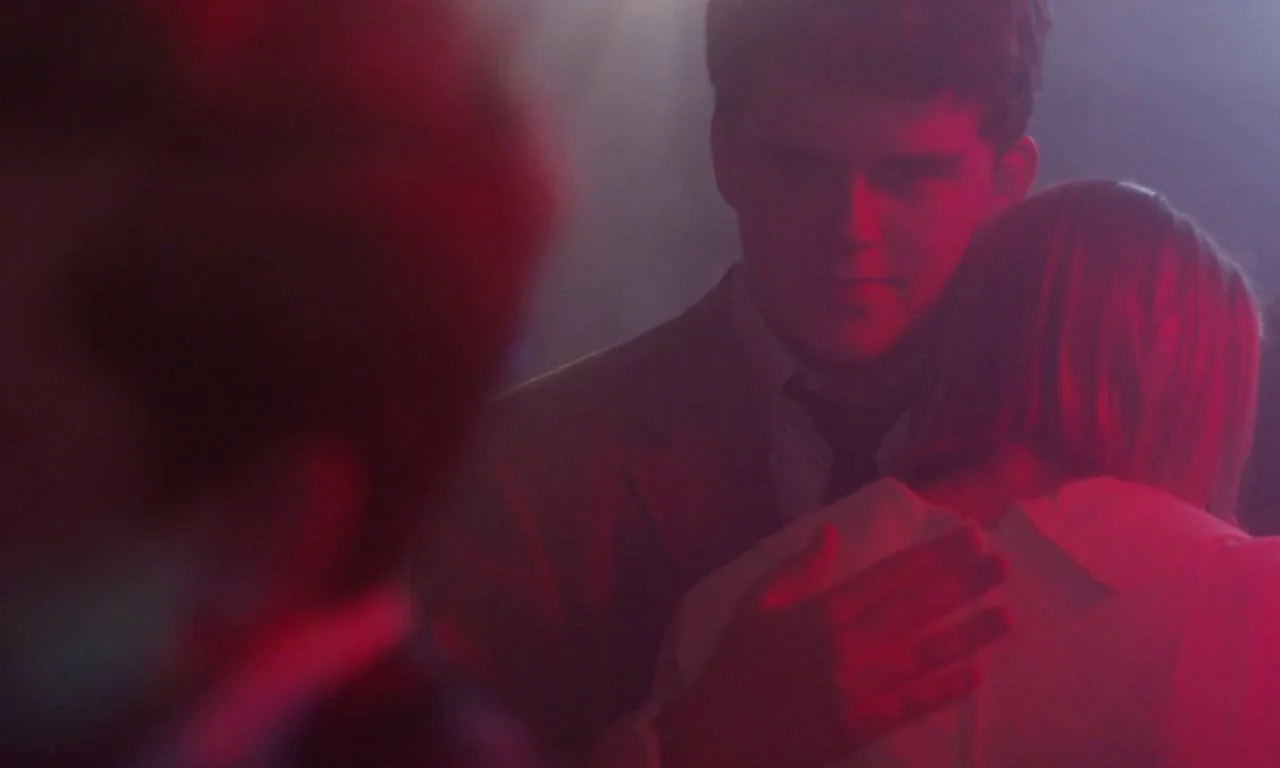 Ham on Rye (2019) movie still: medium — A dark, smoke-filled dance floor is illuminated by intense, saturated red neon lighting. A man in a light…
