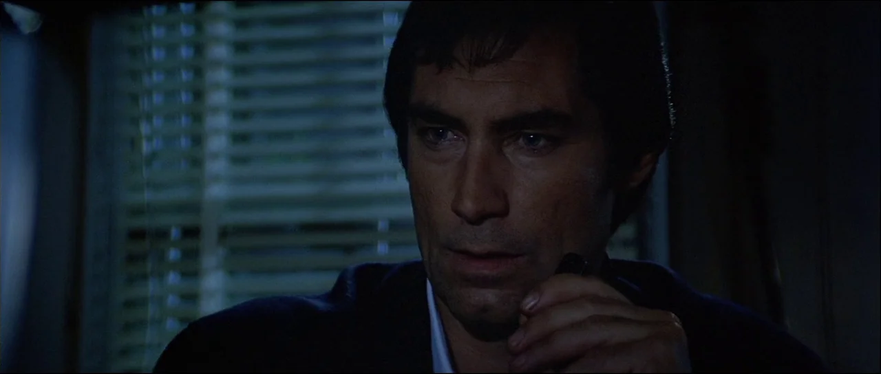 Licence to Kill (1989) movie still: closeup — A dimly lit room features a window with horizontal blinds in the background. A man stands in the…