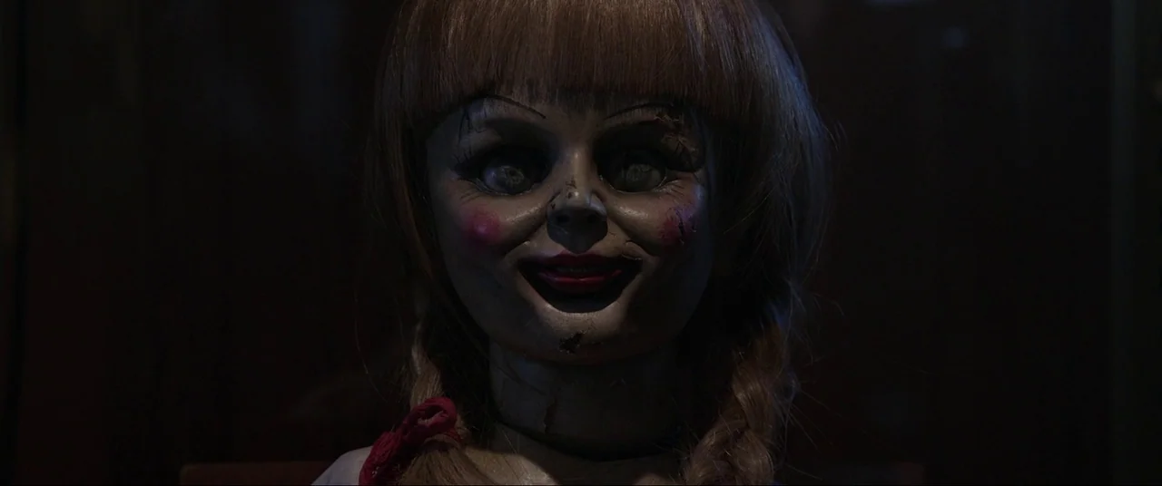 The Conjuring (2013) movie still: closeup — A dark, dimly lit environment obscures the surroundings. An antique porcelain doll stares directly…