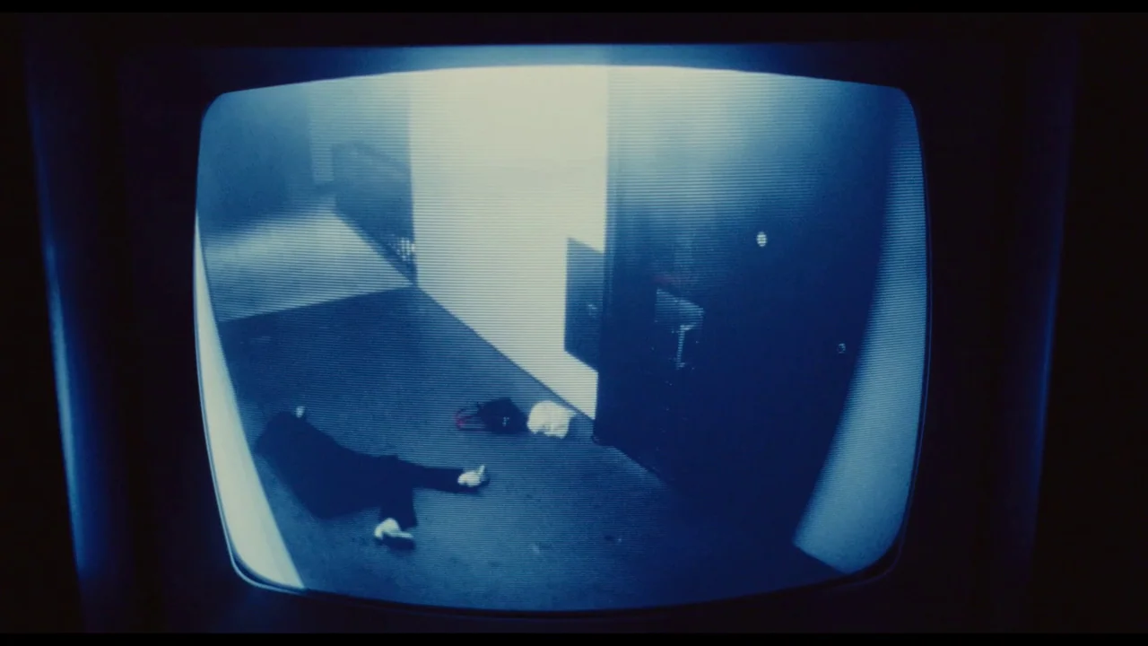 Millennium Mambo (2001) movie still: wide — A dimly lit indoor hallway with a single closed door and a light-colored wall. A single figure lies on…