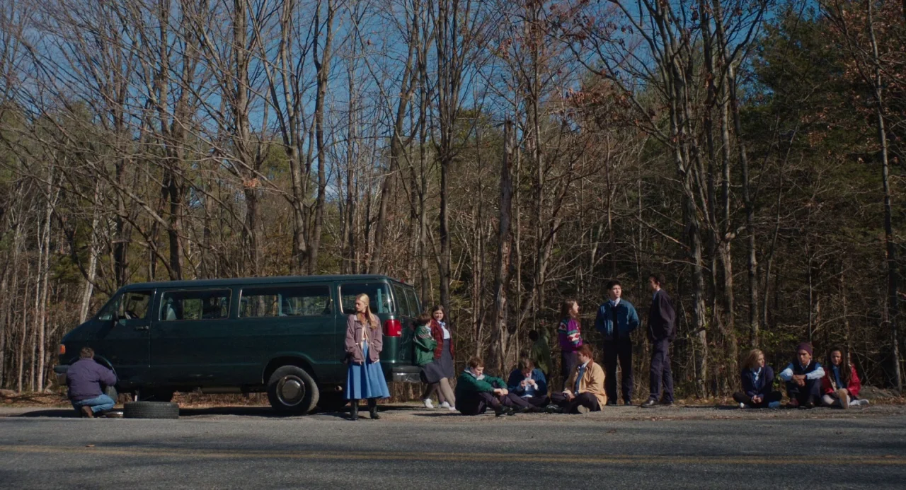 The Miseducation of Cameron Post (2018) movie still: wide — A dark green van sits parked on the shoulder of a paved asphalt road. Several teenagers…