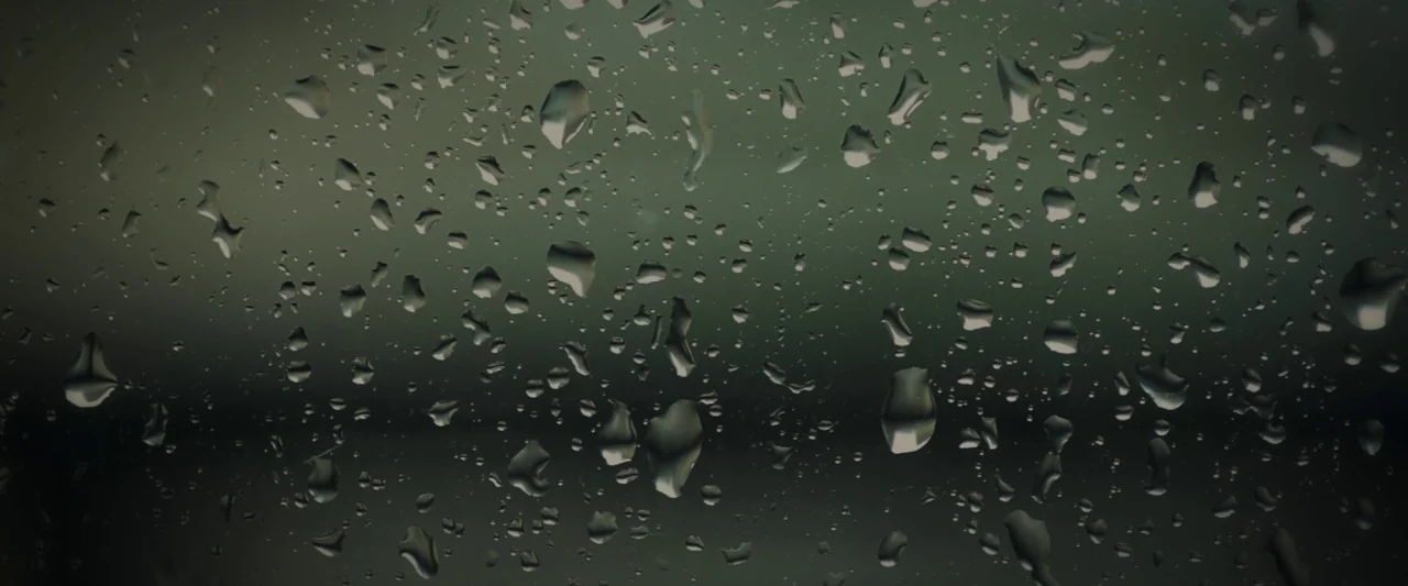 20,000 Days on Earth (2014) movie still: closeup — A dark, blurred surface is covered in scattered droplets of varying sizes. Rain beads cling to…
