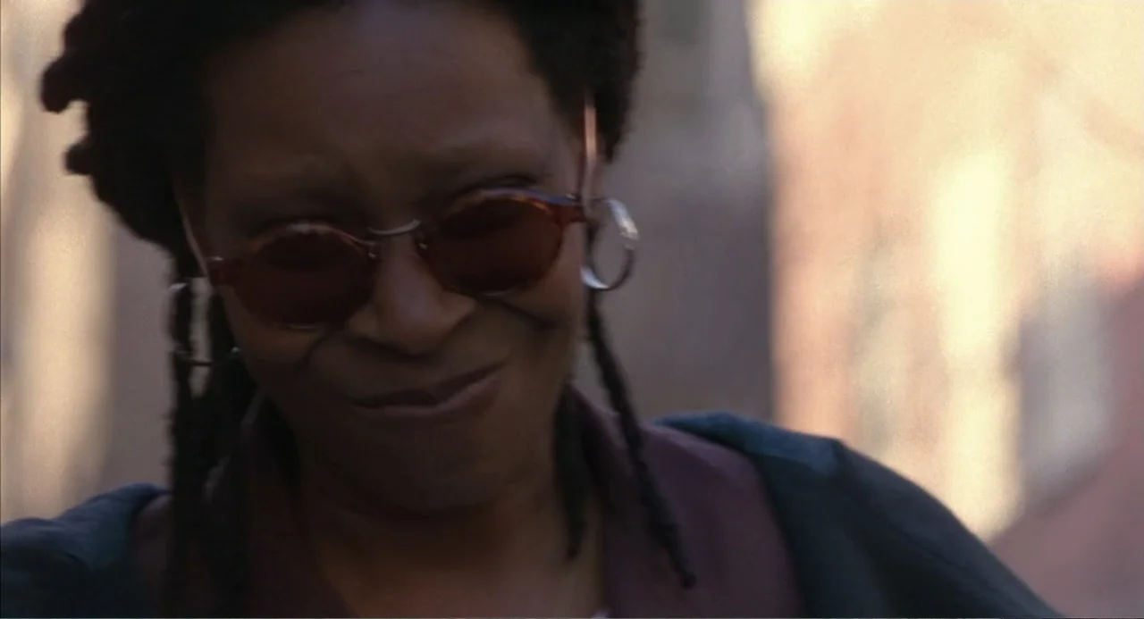 Bogus (1996) movie still: closeup — An urban outdoor setting with blurred architectural elements in the background. A woman with dreadlocks and…