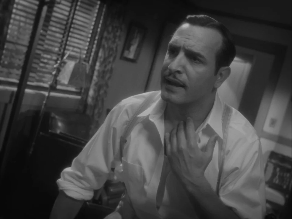 The Artist (2011) movie still: medium — A dimly lit room with blinds over a window in the background. A man touches his throat while looking away…