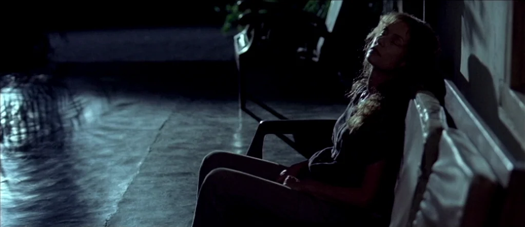 White Material (2009) movie still: medium — A dark outdoor patio at night features a pool edge reflecting dim light. A woman sits on a patio chair…