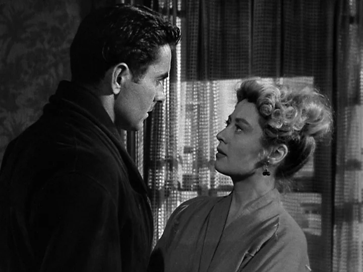 Nightmare Alley (1947) movie still: medium — A domestic interior with dark curtains visible behind the two people in the frame. A man and a woman…