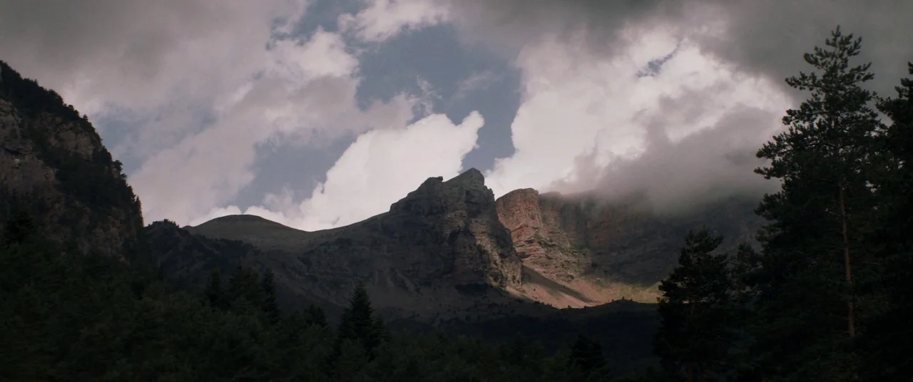 The Sisters Brothers (2018) movie still: establishing — A rugged mountain range with steep rocky cliffs dominates the frame under a cloudy sky.…