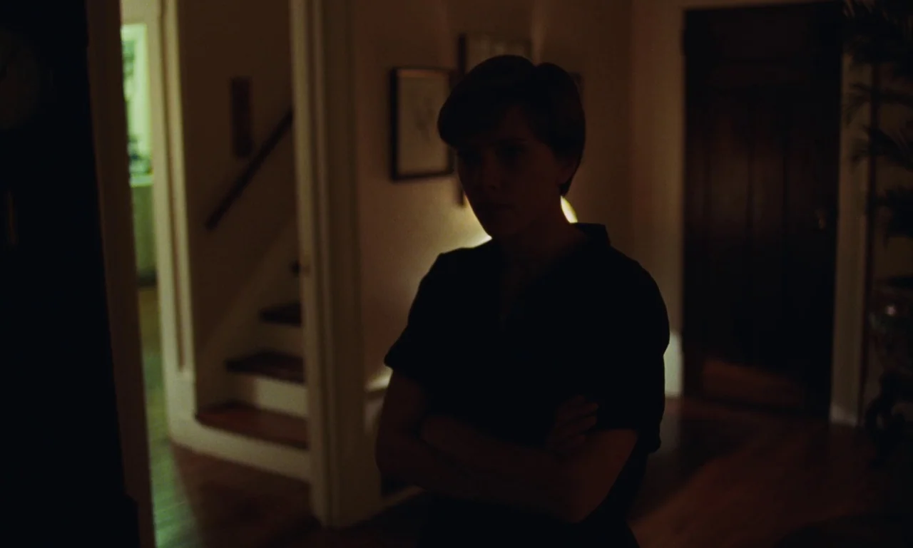 Marriage Story movie still: medium — A dark home interior features a narrow hallway leading to a staircase in back. A woman stands in the mid-ground…