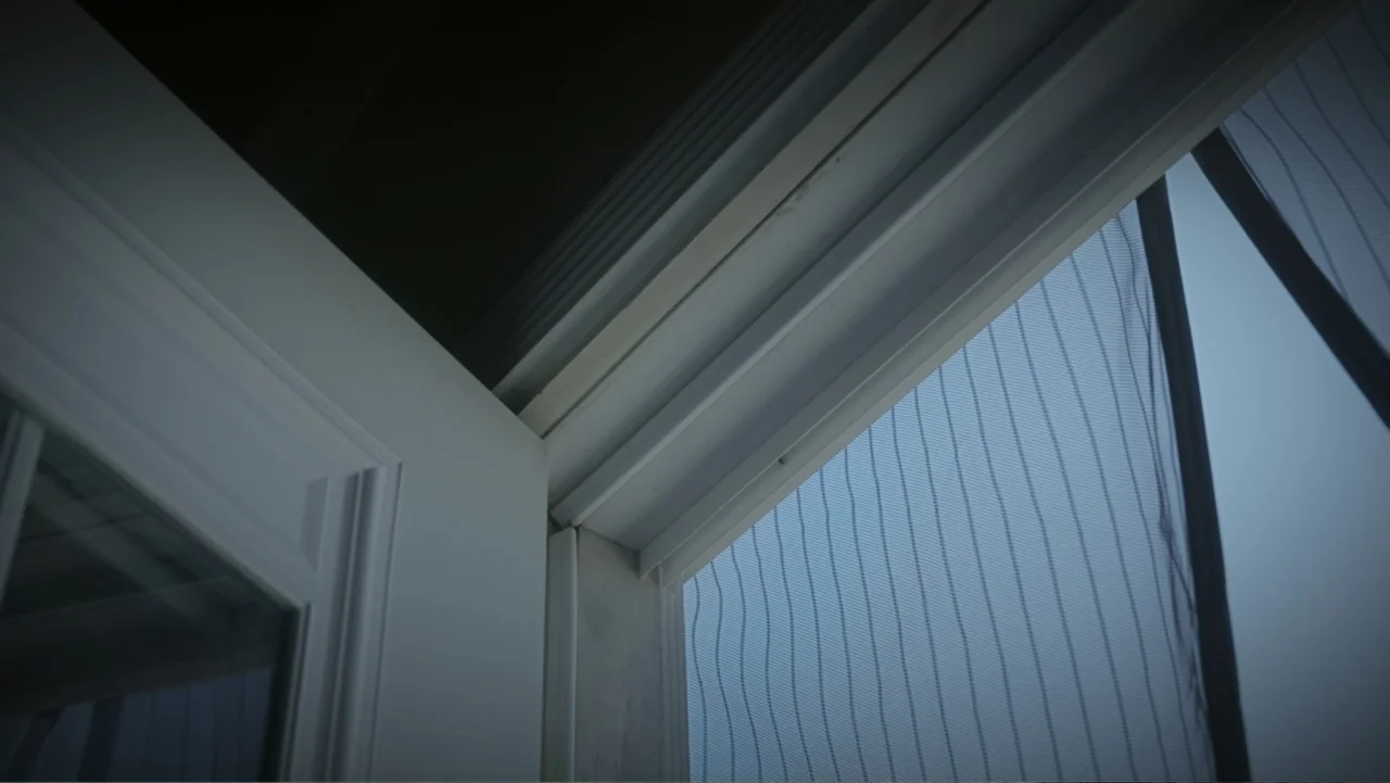 Predators (2010) movie still: establishing — A partially open white door frame borders a fine-meshed screen door. The outdoor light illuminates the…