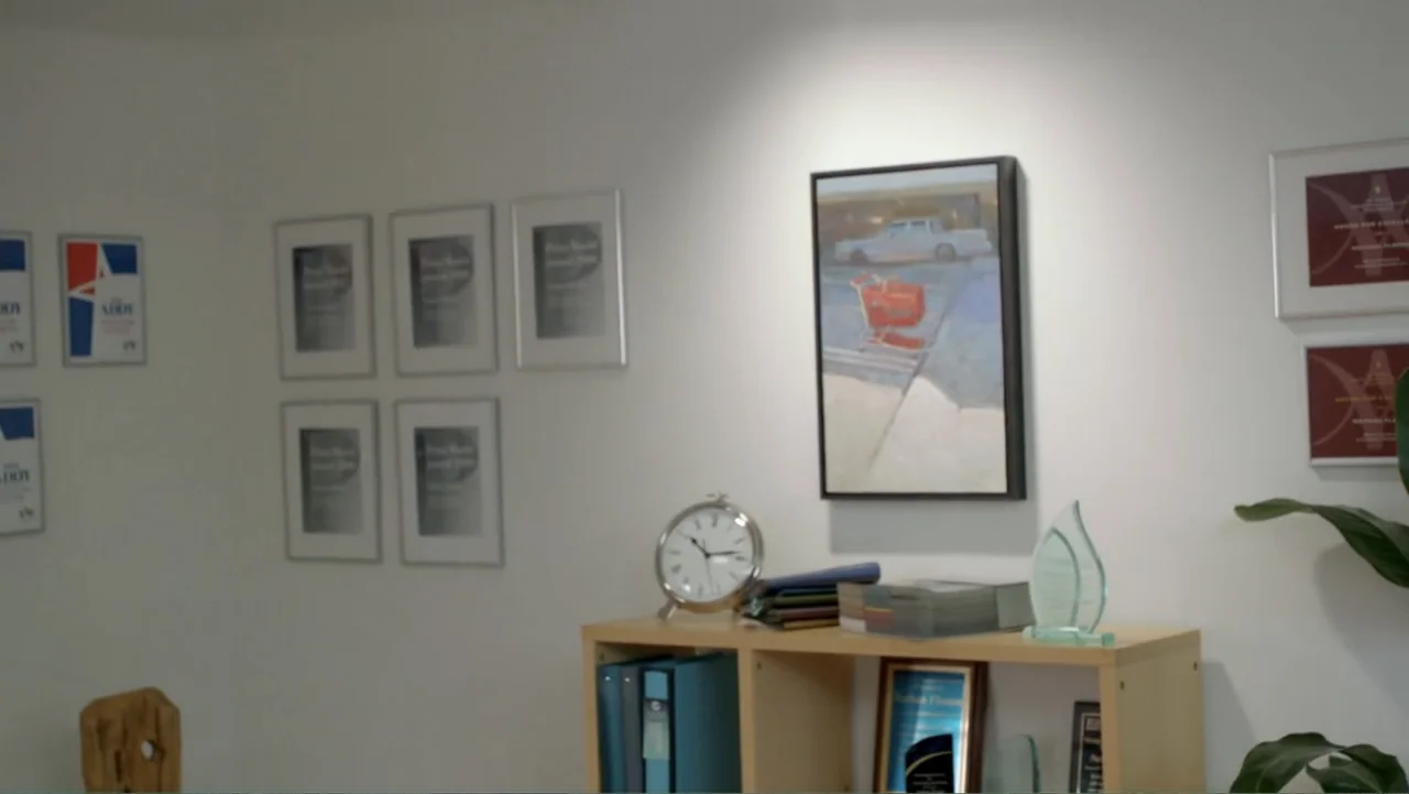 Clear History (2013) movie still: medium — A brightly lit office space features white walls decorated with numerous framed award certificates. A…