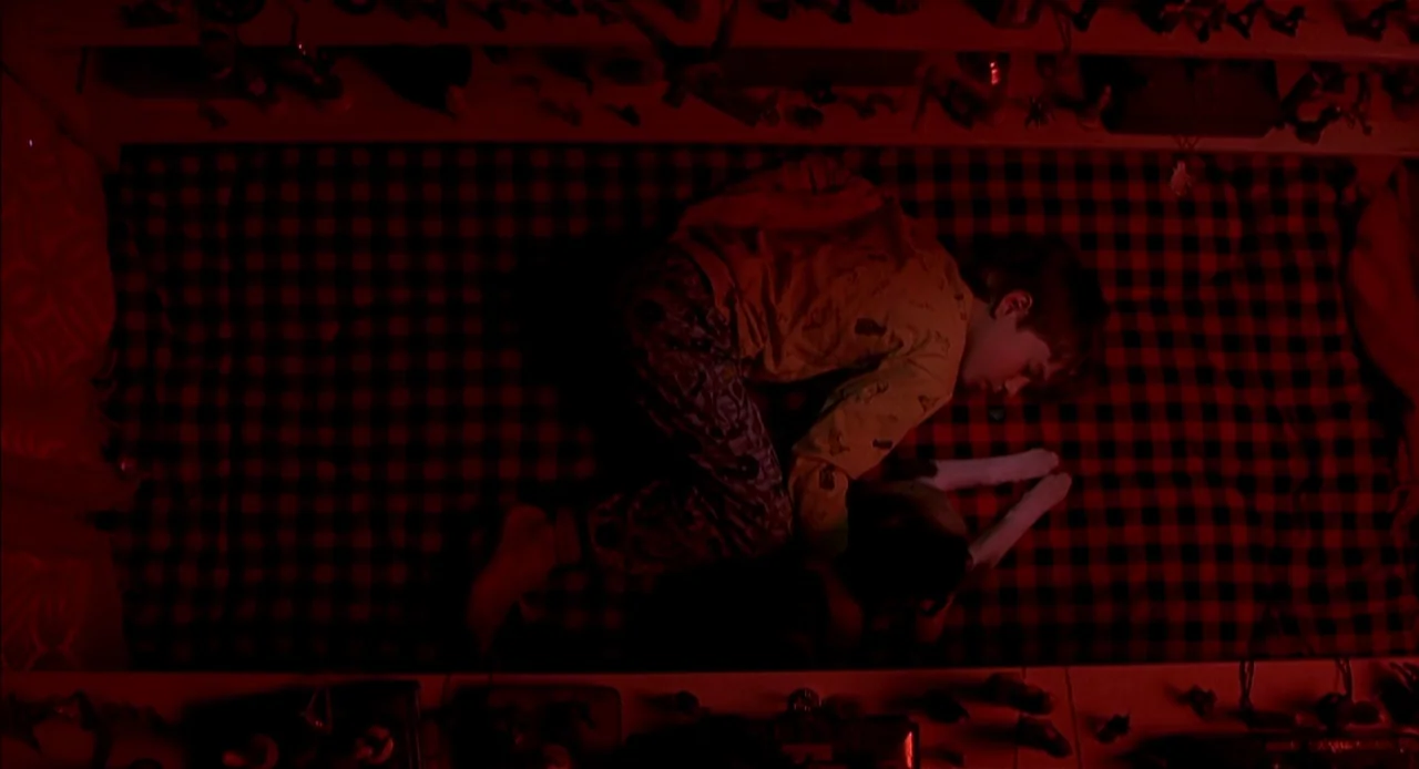 The Sixth Sense (1999) movie still: fullbody — A child rests on a mattress with a red and black checkered pattern. Small toys line the edges of the…