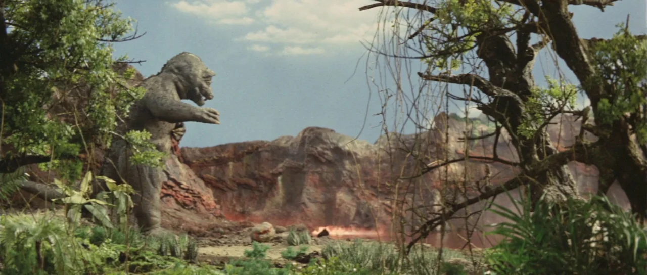 Son of Godzilla (1967) movie still: wide — A rugged volcanic landscape features rocky, jagged cliffs under a partly cloudy blue sky. A large, grey…