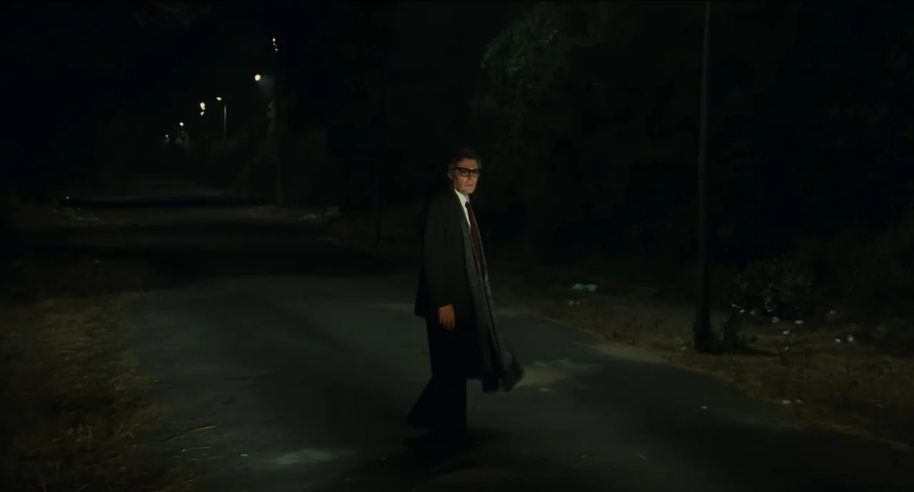 City of Women (1980) movie still: fullbody — A lonely paved road at night is surrounded by dense, dark vegetation and trees. A man in a suit pauses…