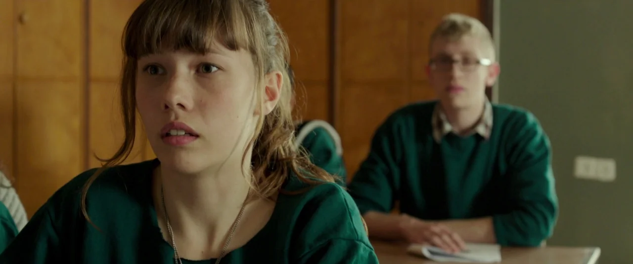 Big Bad Wolves (2013) movie still: medium — A school classroom features wood-paneled walls and rows of wooden student desks. A young woman and a…