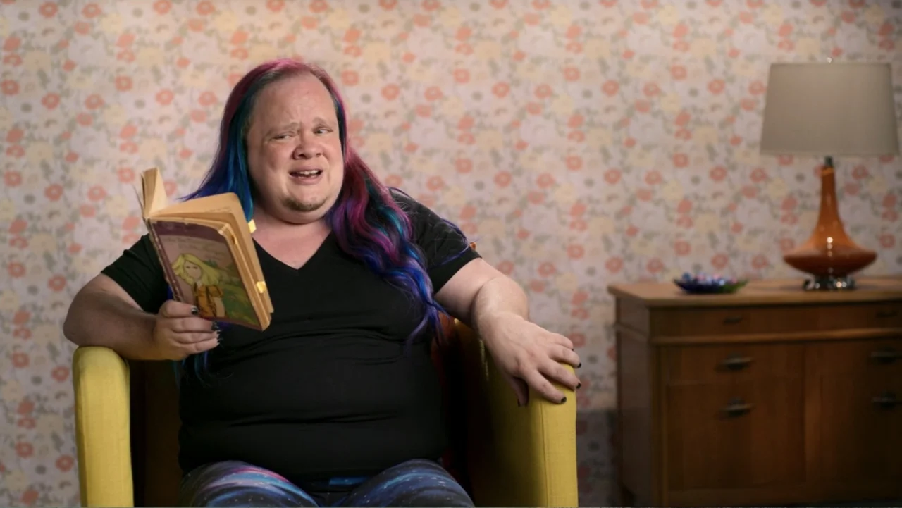 Judy Blume Forever (2023) movie still: medium — A person sits in a bright yellow chair against a vintage floral wallpaper background. The individual…