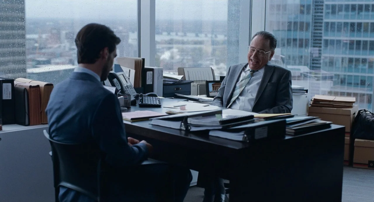 Matthias & Maxime (2019) movie still: medium — A high-rise executive office with a panoramic city view through rain-streaked windows. An older man…