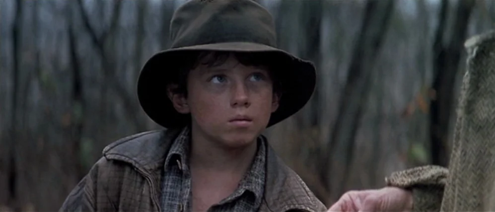 The People vs. Larry Flint (1996) movie still: closeup — A young boy stands in a densely wooded area with bare, leafless trees. He is wearing a…